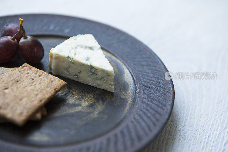 在白色木桌上，Fourme D'Ambert奶酪放在饼干和红葡萄的盘子上